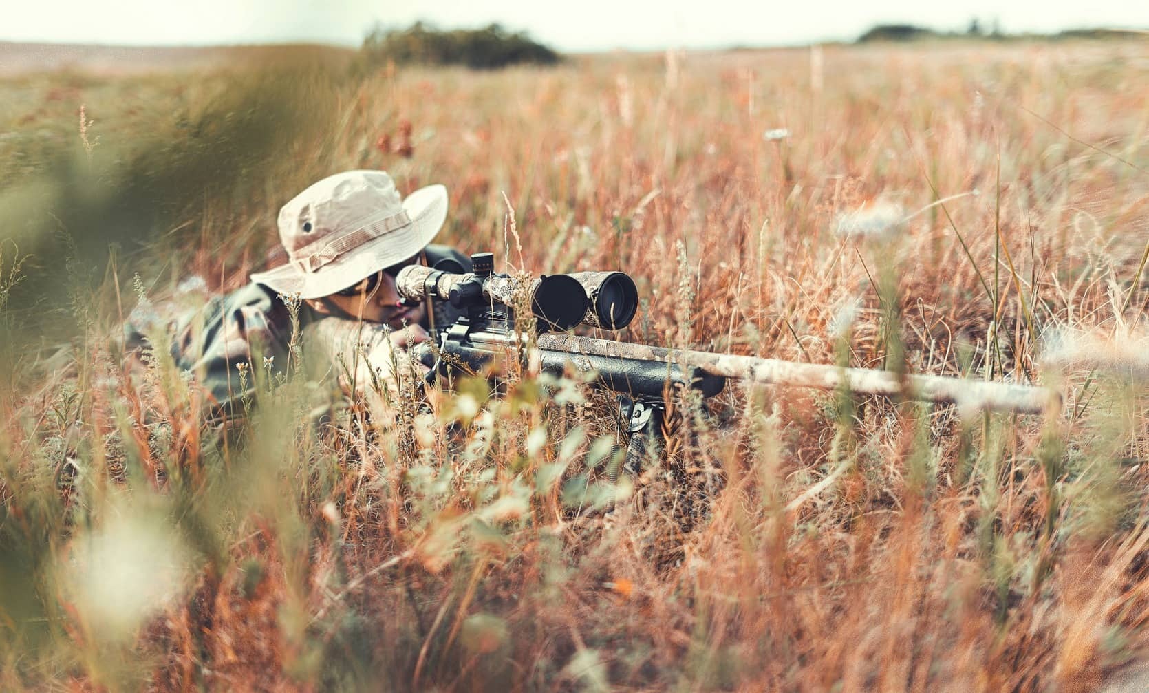Outdoor Gear Shop -Outdoor Gear Shop man in tall grass aiming hunting rifle with accessories
